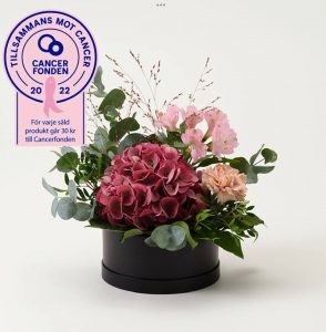 Liten rund hattask med vacker blomsterdekoration i lila/rosa. Beställ hos Interflora!