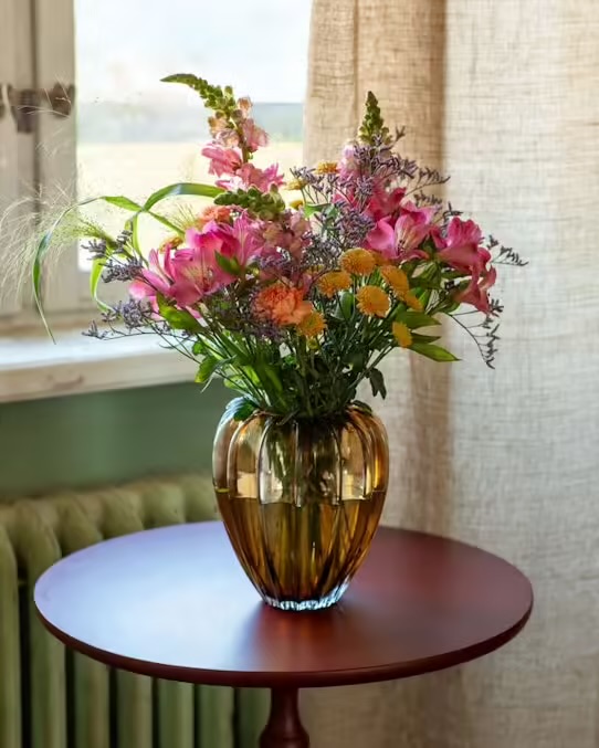 Interfloras vackra augustibukett. Den går i rosa, cerise, grönt, gult och aprikost. Blommor i buketten: lejongap, alstroemeria, nejlika, krysantemum och blandat grönt.